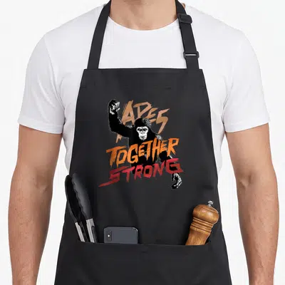 Rise ape apron - Black chimpanzee with distressed orange and red TOGETHER STRONG text overlay — shown on a black cotton canvas apron against a white background