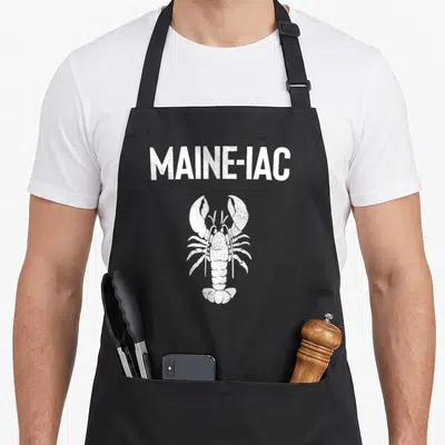 Maine fishing aprons - White distressed MAINE-IAC text above a white lobster illustration on a dark background — shown on a black cotton canvas apron against a white background