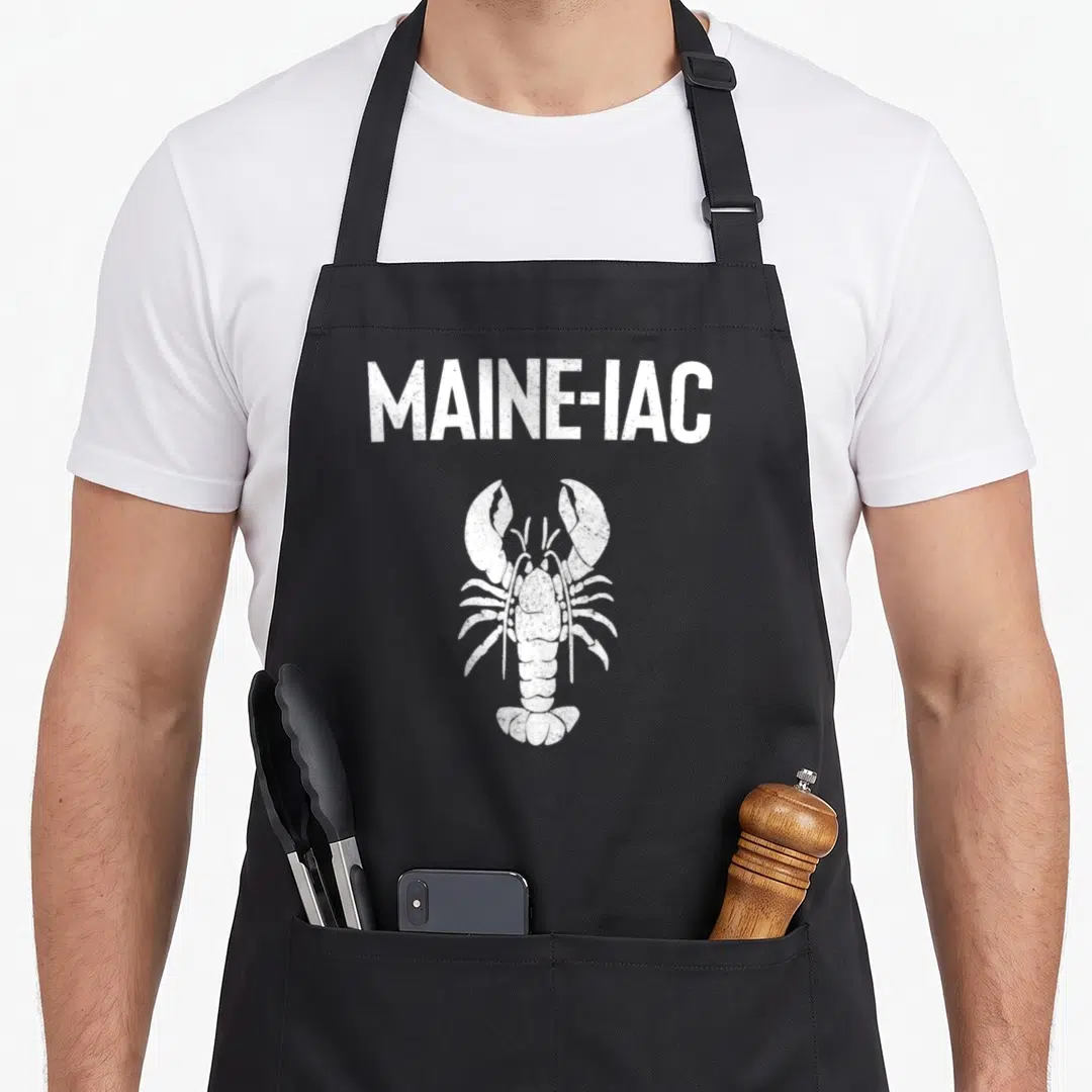 Maine fishing aprons - White distressed MAINE-IAC text above a white lobster illustration on a dark background — shown on a black cotton canvas apron against a white background