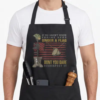 Risk memorial day apron - Soldier helmet rifle boots with distressed flag and memorial text in red yellow grey tan green — shown on a black cotton canvas apron against a white background