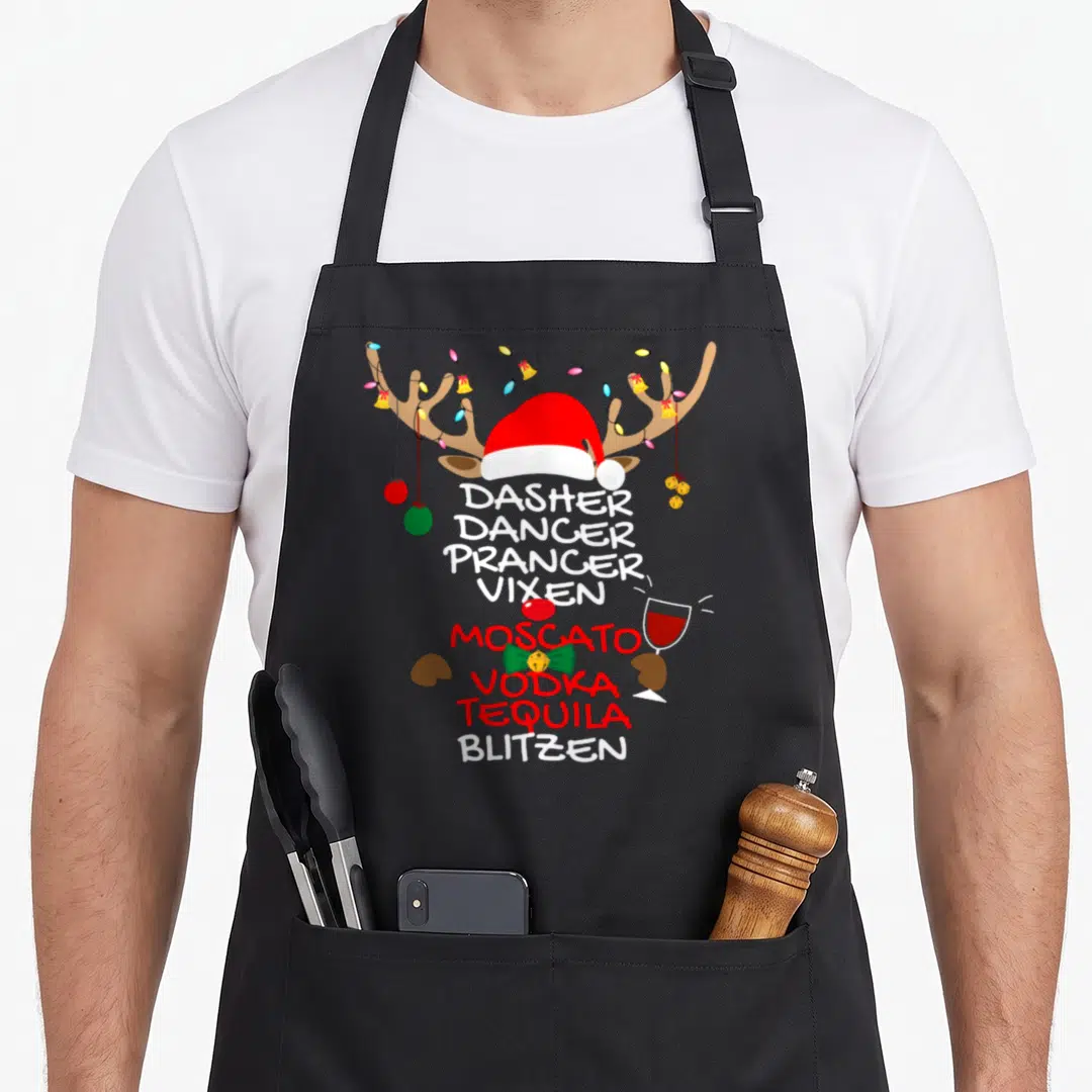 Vixen moscato apron - Cartoon reindeer head with Santa hat, antler lights, and stacked text listing Dasher Dancer — shown on a black cotton canvas apron against a white background
