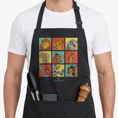 Grid character aprons - Nine square cartoon portraits of The Lion King characters in orange, yellow, blue, red — shown on a black cotton canvas apron against a white background