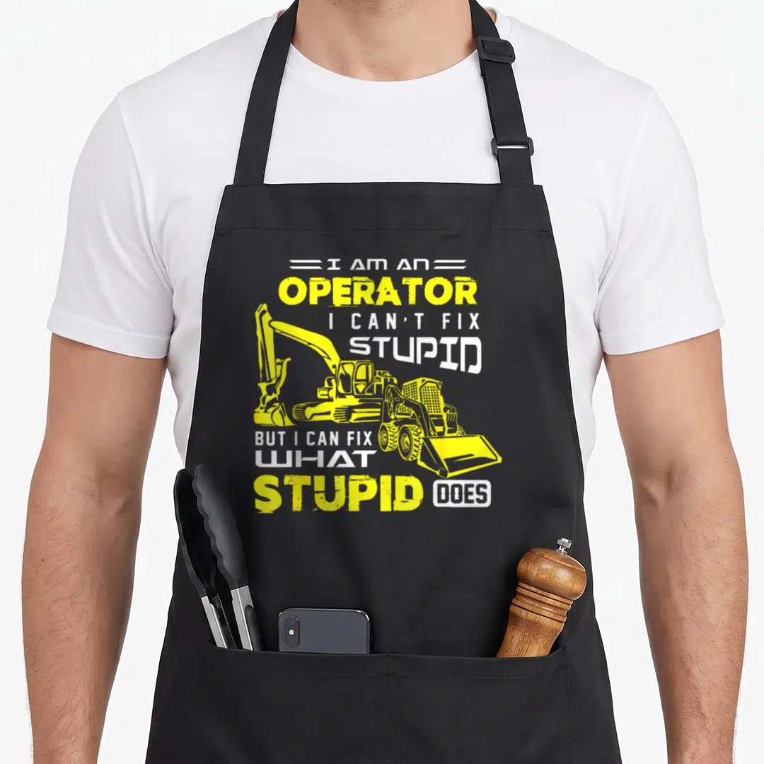 Machinery heavy apron - Yellow excavator and skid steer loader with white and yellow distressed text reading I am — shown on a black cotton canvas apron against a white background