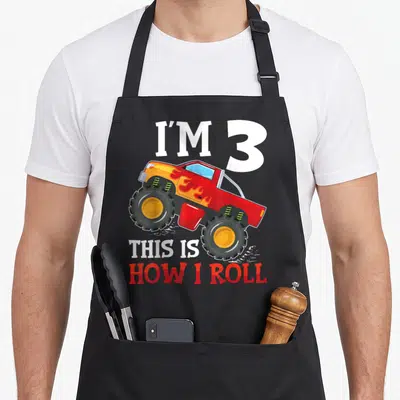 3yr truck apron - Monster truck illustration with I'M 3 THIS IS HOW I ROLL text — shown on a black cotton canvas apron against a white background