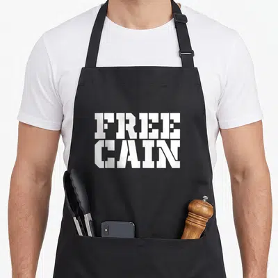Free cabin lover apron - White block letters reading FREE CAIN stacked vertically on grey background — shown on a black cotton canvas apron against a white background
