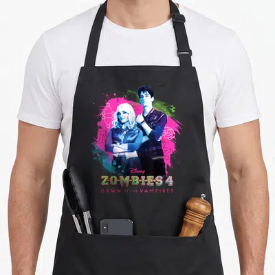 Dawn zombie apron - Two people standing centrally against pink blue and green paint splashes with stacked movie text — shown on a black cotton canvas apron against a white background
