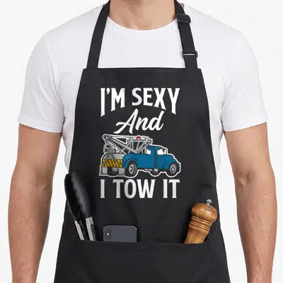 Operator driver truck apron - Blue cartoon tow truck with I'M SEXY And I TOW IT text — shown on a black cotton canvas apron against a white background