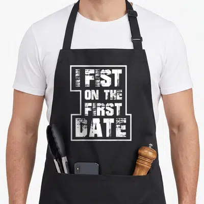 Fist offensive aprons - White distressed text reading I FIST ON THE FIRST DATE inside a broken rectangular border — shown on a black cotton canvas apron against a white background