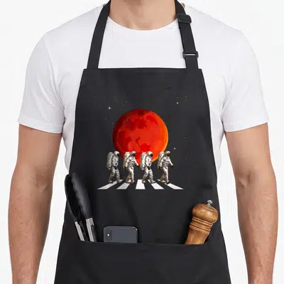 Spaceman walking apron - Four astronauts walking on white stripes in front of a red planet and stars — shown on a black cotton canvas apron against a white background