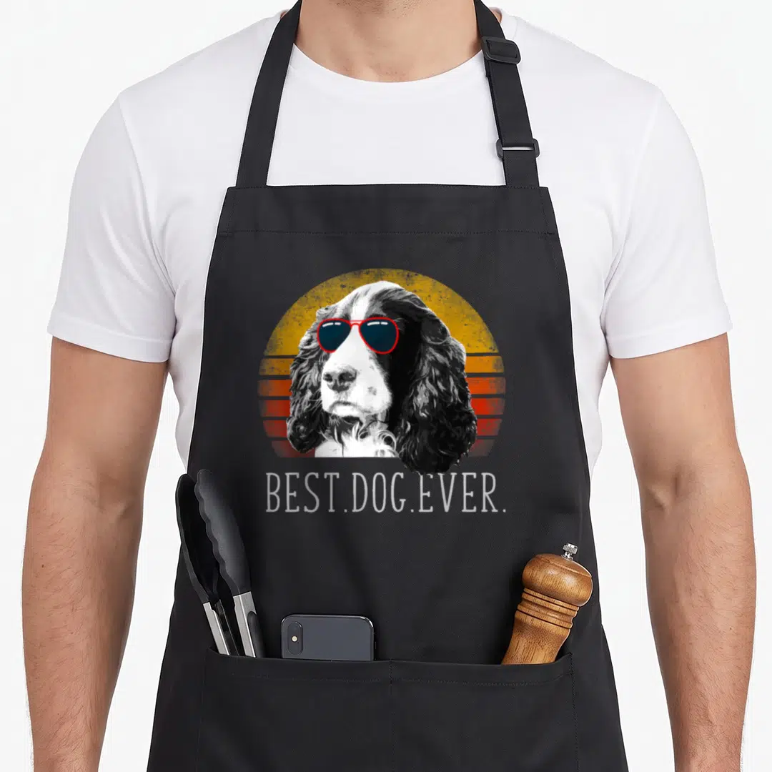 Spaniel english apron - Dog with red sunglasses in front of yellow and orange striped sun with BEST.DOG.EVER text — shown on a black cotton canvas apron against a white background