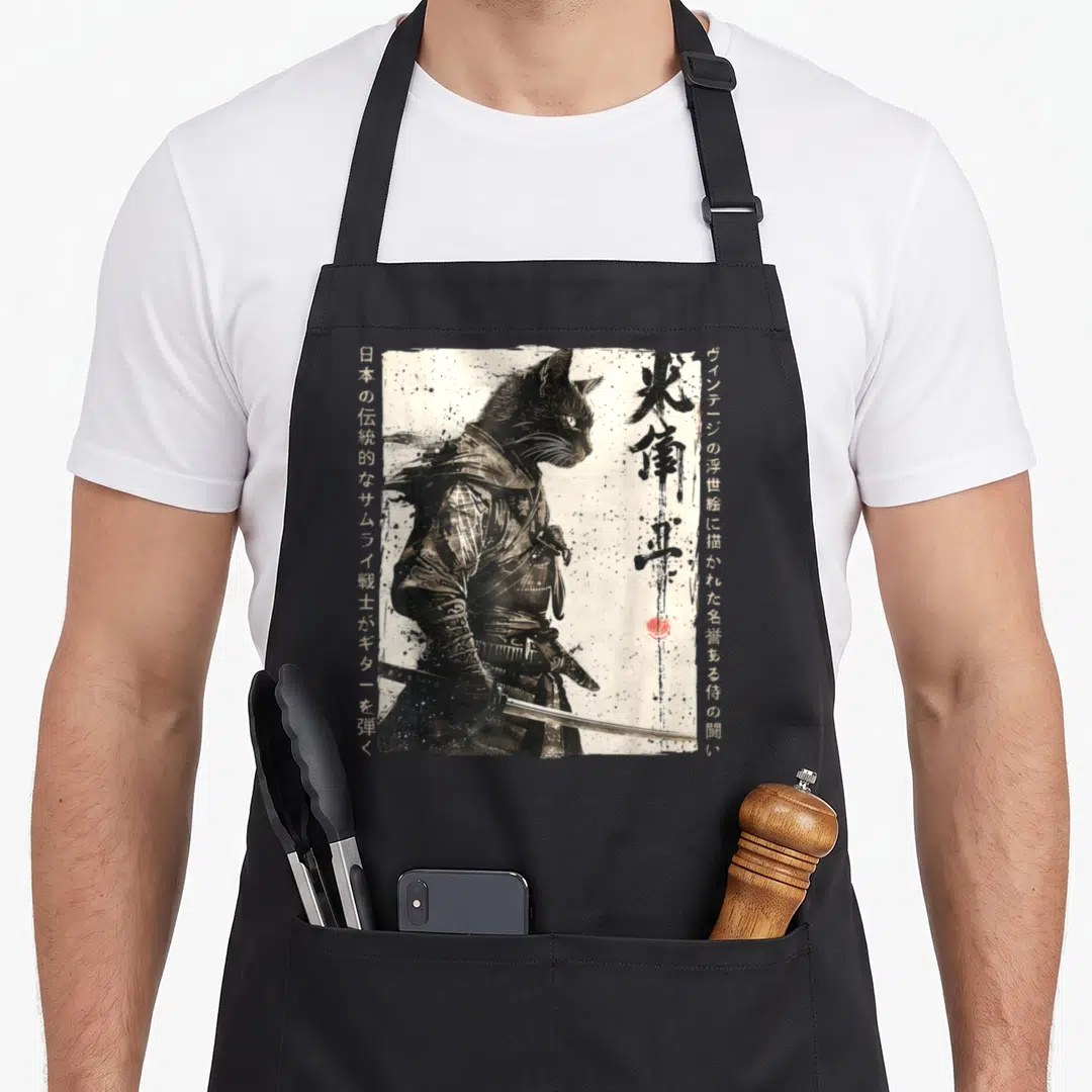 Ukiyo cat apron - Black cat samurai in armor holding katana with vertical Japanese text and red seal stamp — shown on a black cotton canvas apron against a white background