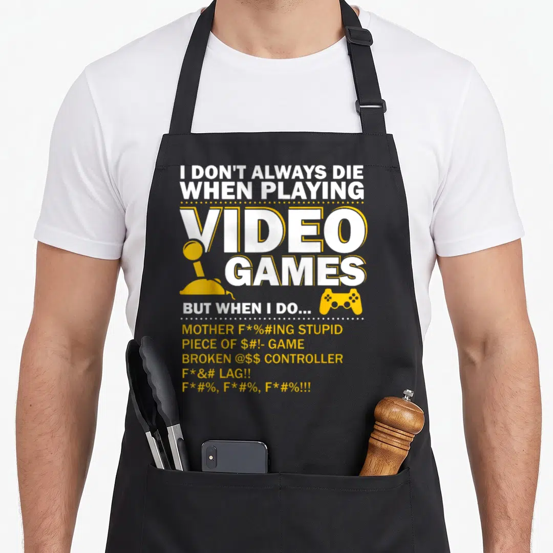 Playing gaming apron - White and yellow text reading I DON'T ALWAYS DIE with joystick and gamepad icons — shown on a black cotton canvas apron against a white background