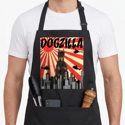 Japanese doberman pinscher apron - Giant black and tan Doberman named DOGZILLA towering over grey city skyline — shown on a black cotton canvas apron against a white background