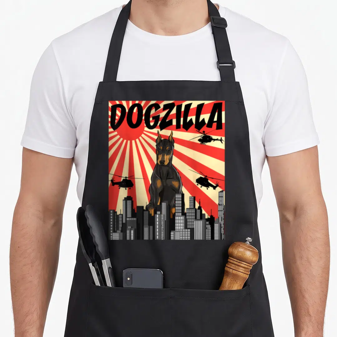 Japanese doberman pinscher apron - Giant black and tan Doberman named DOGZILLA towering over grey city skyline — shown on a black cotton canvas apron against a white background
