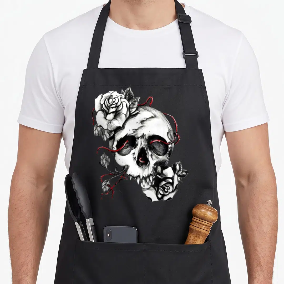 Skull rose apron - Line art skull with two white roses and red thorns piercing eye sockets — shown on a black cotton canvas apron against a white background