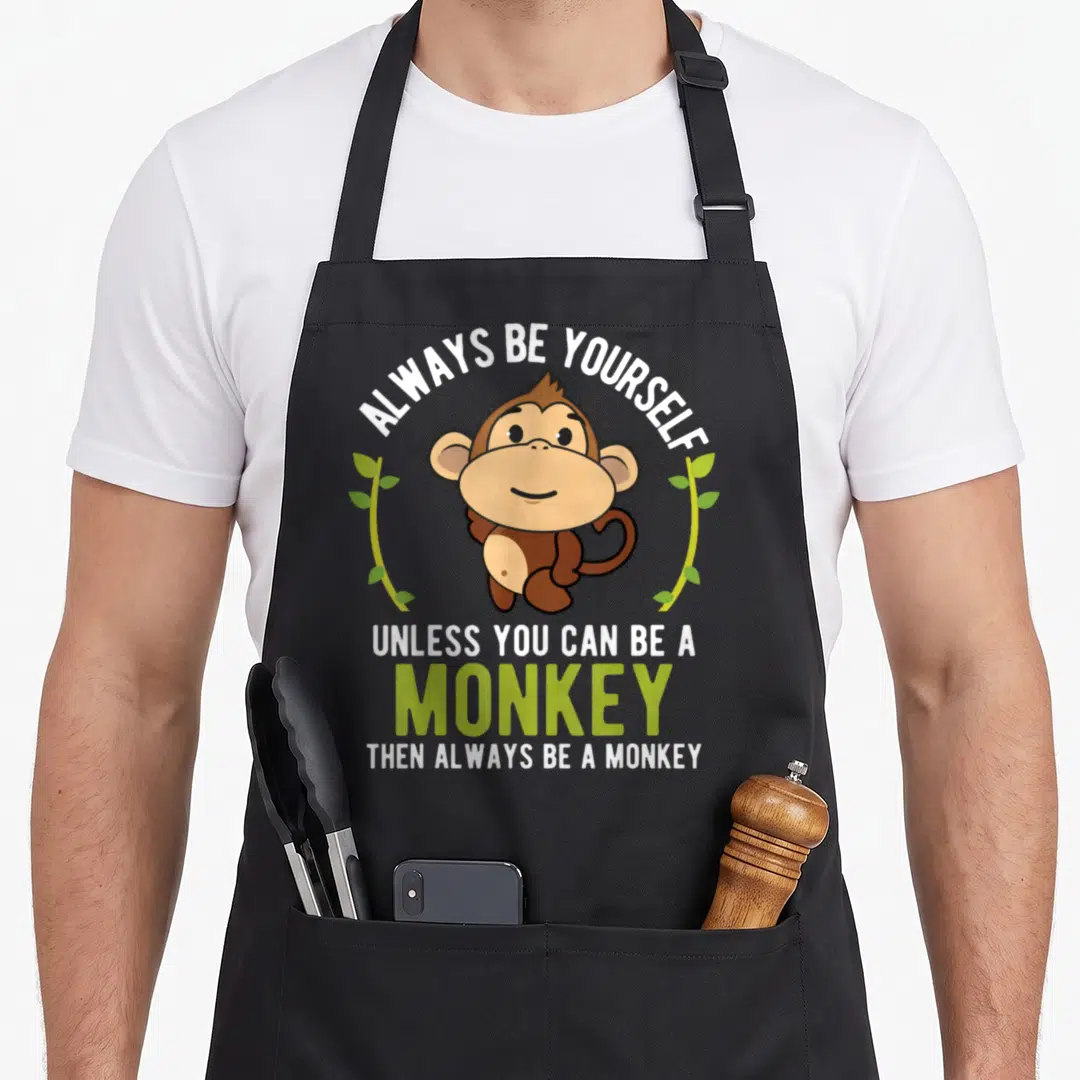 Yourself funny monkey saying quote apron - Cartoon brown monkey with white and lime green text ALWAYS BE YOURSELF — shown on a black cotton canvas apron against a white background