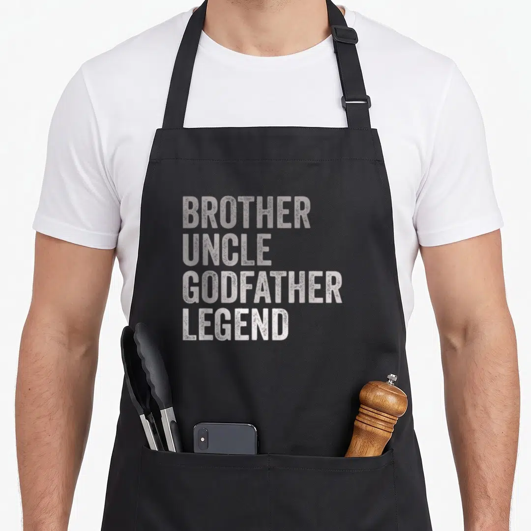 Brother godfather apron - White stacked text reading BROTHER UNCLE GODFATHER LEGEND on grey background — shown on a black cotton canvas apron against a white background