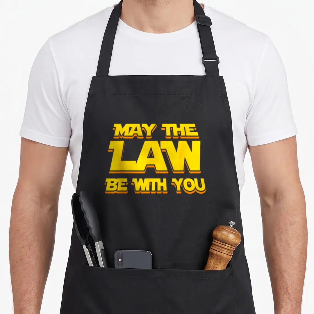 May lawyer apron - Stacked yellow text MAY THE LAW BE WITH YOU with orange outlines — shown on a black cotton canvas apron against a white background