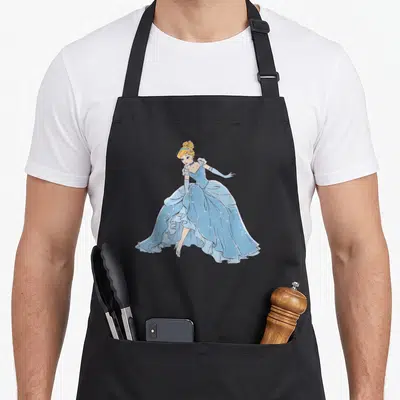 Ballgown cinderella apron - Cartoon blonde woman in light blue ballgown lifting skirt to reveal silver slipper — shown on a black cotton canvas apron against a white background