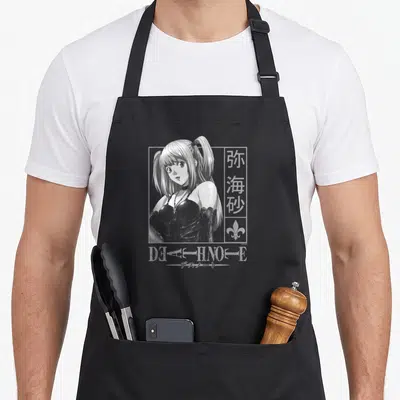 Misa anime apron - Woman in rectangular frame with kanji, fleur-de-lis, and DEATH NOTE text in white and grey — shown on a black cotton canvas apron against a white background