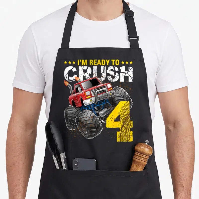 Crush monster truck apron - Red monster truck with yellow number 4 and cracked text reading I'm Ready to Crush — shown on a black cotton canvas apron against a white background