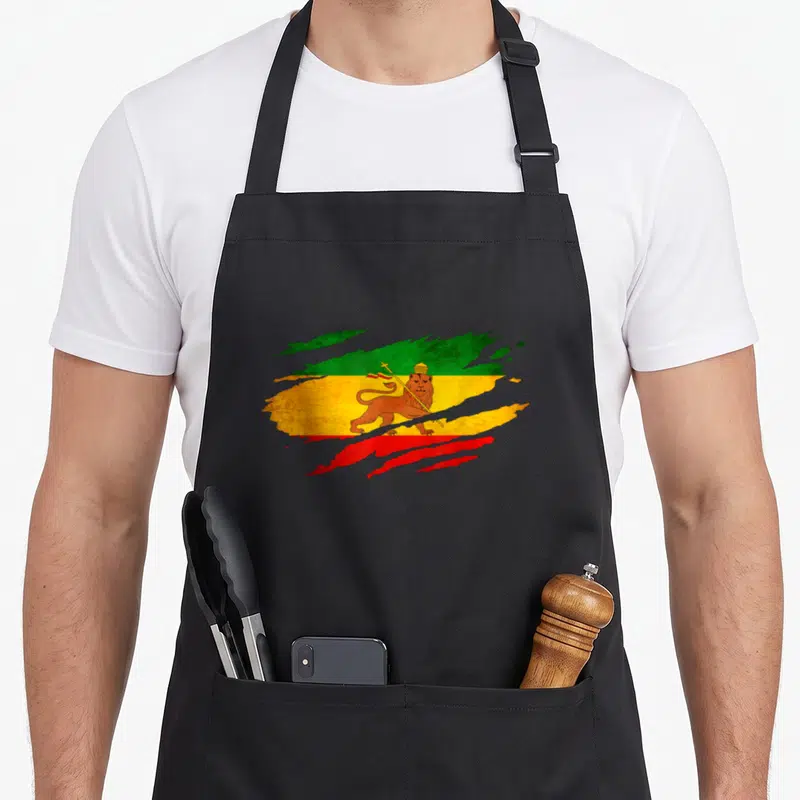 Ethiopia lion apron - Distressed green yellow red flag with crowned lion holding a staff — shown on a black cotton canvas apron against a white background