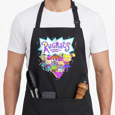 Geometric novelty apron - Rugrats text in burst above five cartoon babies in purple blue yellow pink — shown on a black cotton canvas apron against a white background