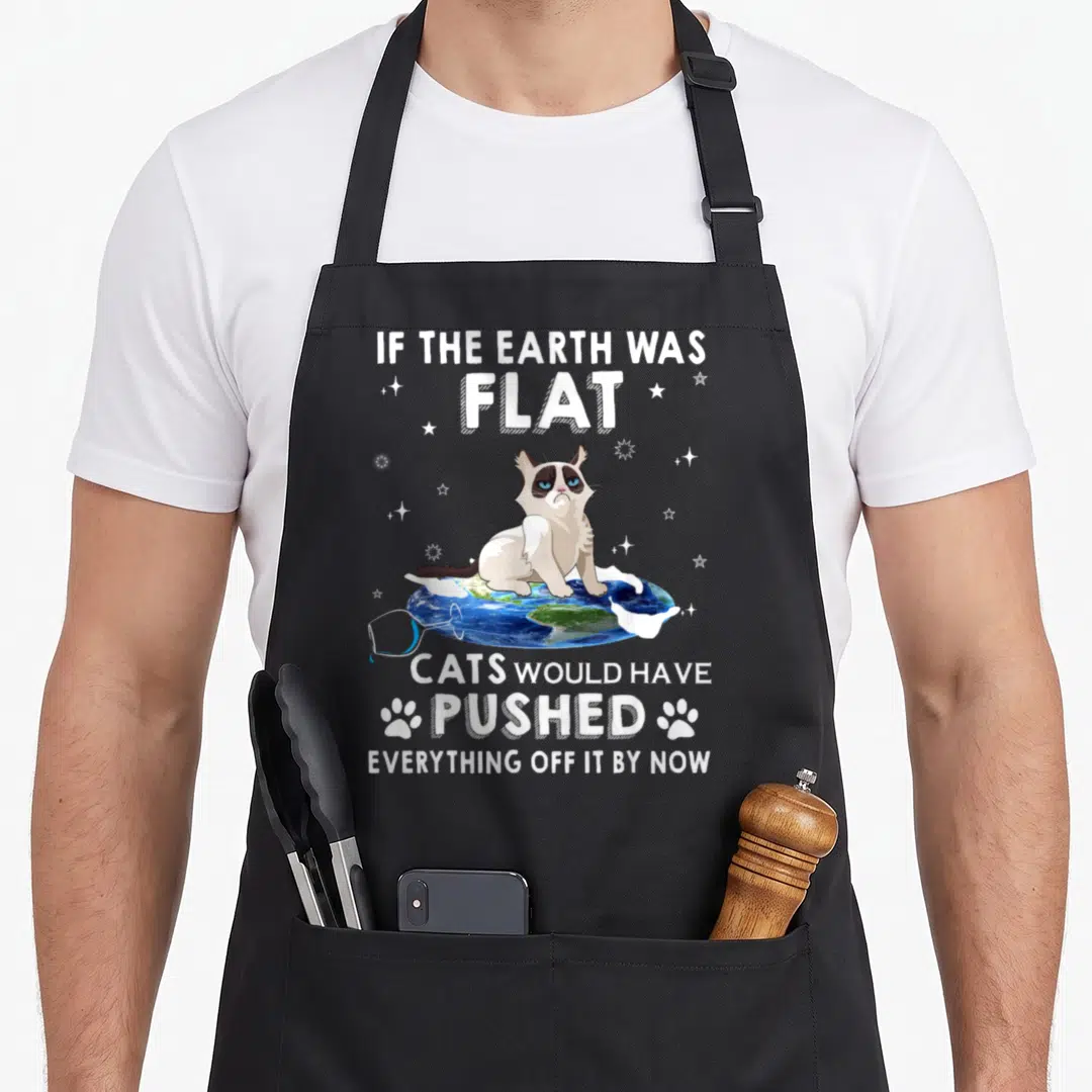 Flat cat apron - Cartoon cat on flat earth disk with text about pushing everything off by now — shown on a black cotton canvas apron against a white background