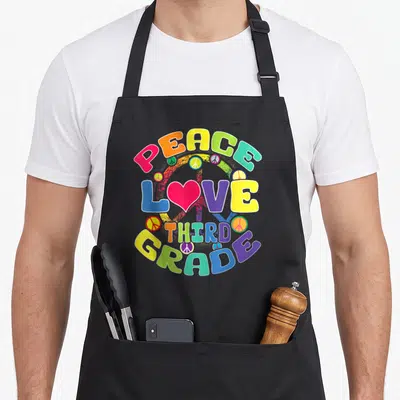 Peace classroom aprons - Stacked colorful text PEACE LOVE THIRD GRADE with pink heart and peace signs — shown on a black cotton canvas apron against a white background