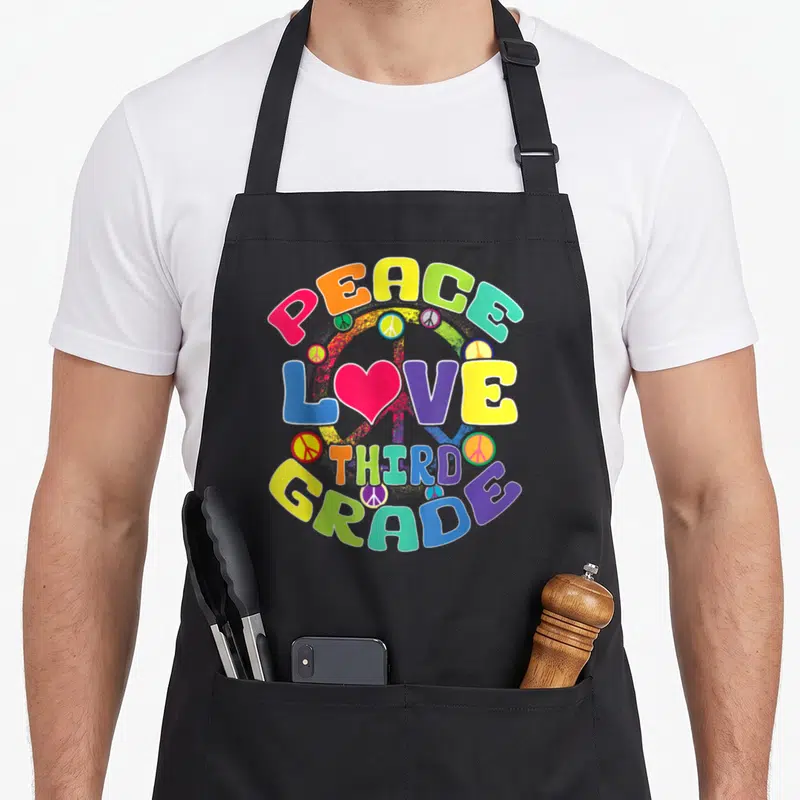 Peace classroom aprons - Stacked colorful text PEACE LOVE THIRD GRADE with pink heart and peace signs — shown on a black cotton canvas apron against a white background