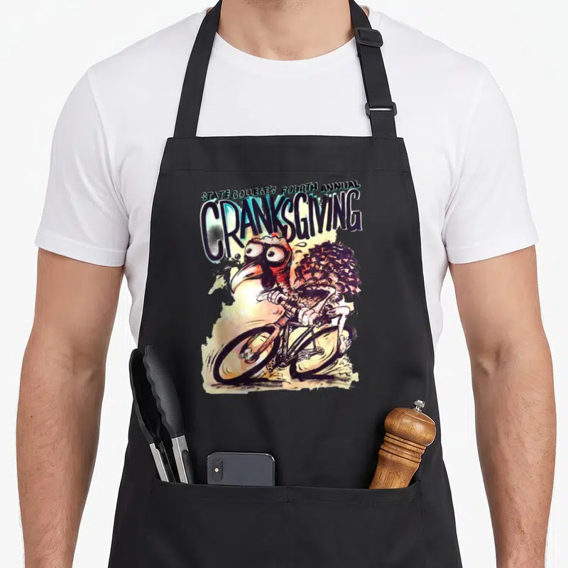 4th state college apron - Stacked text above a cartoon turkey riding a bicycle with wide eyes and sweat drops — shown on a black cotton canvas apron against a white background