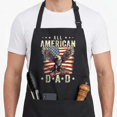 Eagle 4th father day apron - Bald eagle with spread wings on distressed usa flag with all american dad text and stars — shown on a black cotton canvas apron against a white background