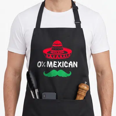 Mustache mexican apron - Red sombrero above white 0% MEXICAN text and a green handlebar mustache — shown on a black cotton canvas apron against a white background