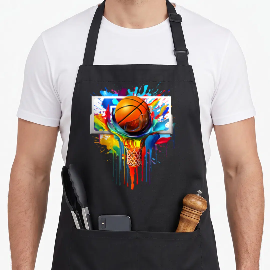 Colorful tie dye apron - Orange basketball and net dissolving into multicolored paint drips on a white backboard — shown on a black cotton canvas apron against a white background