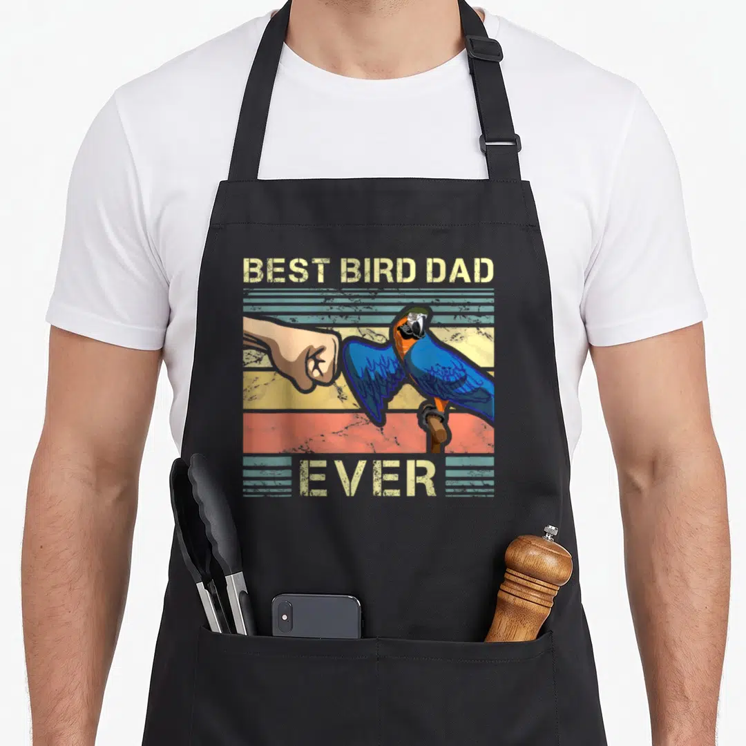 Father bird apron - Retro macav fist bumping human hand with BEST BIRD DAD EVER text on striped background — shown on a black cotton canvas apron against a white background