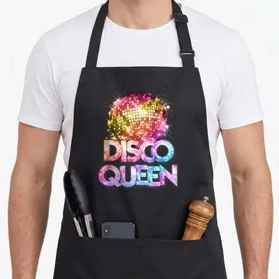 Themed 70s apron - Disco ball and text filled with pink blue yellow purple mirrored tile pattern — shown on a black cotton canvas apron against a white background