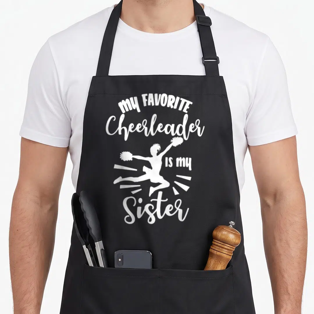 Squad cheerleading apron - White jumping cheerleader silhouette surrounded by My Favorite Cheerleader Is My Sister text — shown on a black cotton canvas apron against a white background