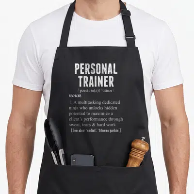 Definition personal apron - White dictionary definition text for Personal Trainer on black fabric — shown on a black cotton canvas apron against a white background
