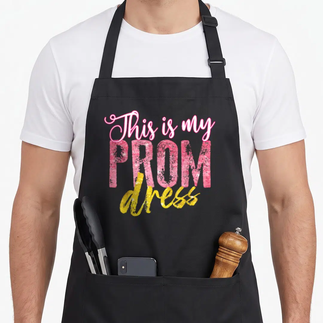 School prom apron - Stacked pink and yellow glitter text reading This is my PROM dress — shown on a black cotton canvas apron against a white background