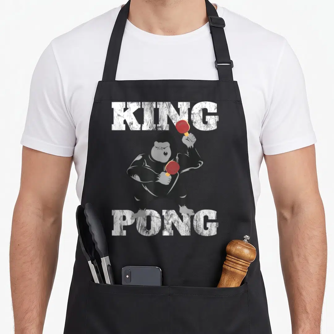 Distressed table apron - Cartoon gorilla holding red paddles between white KING and PONG text — shown on a black cotton canvas apron against a white background