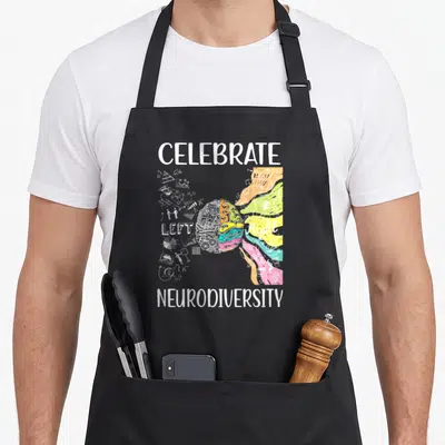 Celebrate adhd awareness apron - Split brain graphic with CELEBRATE NEURODIVERSITY text, grey technical sketches — shown on a black cotton canvas apron against a white background