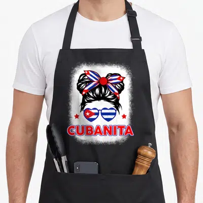 Cubanita cuba hispanic aprons - Cartoon woman with bun, heart sunglasses, red stars, CUBANITA text — shown on a black cotton canvas apron against a white background