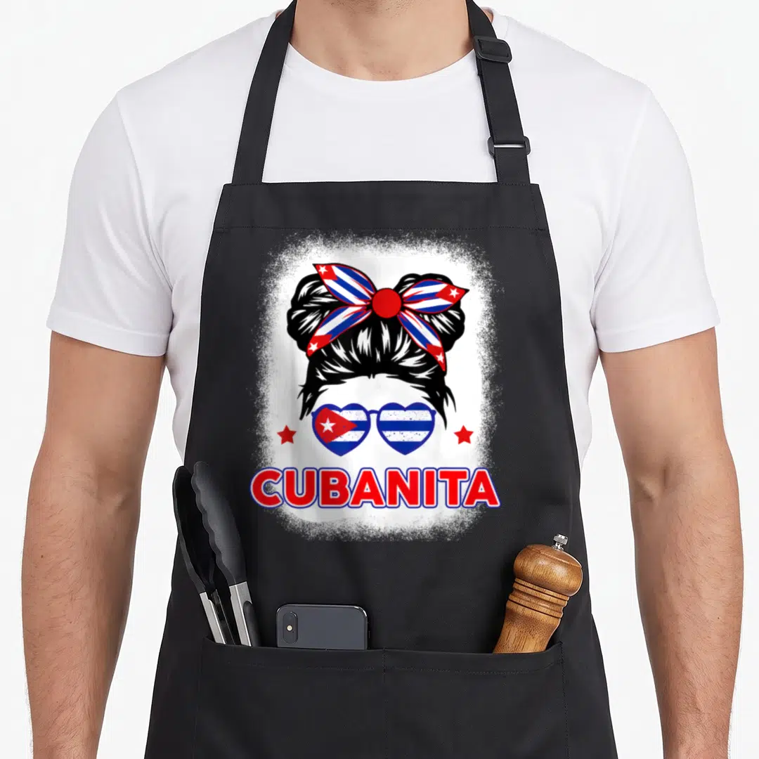 Cubanita cuba hispanic aprons - Cartoon woman with bun, heart sunglasses, red stars, CUBANITA text — shown on a black cotton canvas apron against a white background