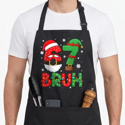Bruh christmas elf apron - Number 67 dressed as Santa and elf with BRUH text and Christmas lights — shown on a black cotton canvas apron against a white background