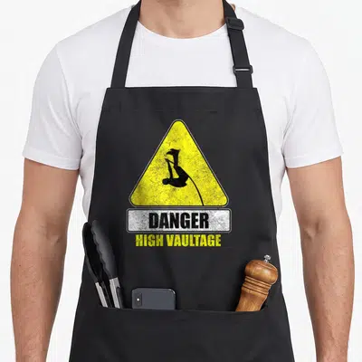 Danger track apron - Yellow warning sign with pole vaulter silhouette and DANGER HIGH VAULTAGE text — shown on a black cotton canvas apron against a white background