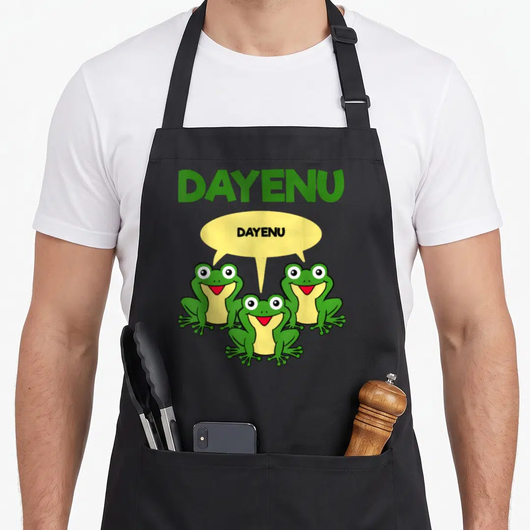 Three passover apron - Three green cartoon frogs with yellow speech bubble saying Dayenu — shown on a black cotton canvas apron against a white background