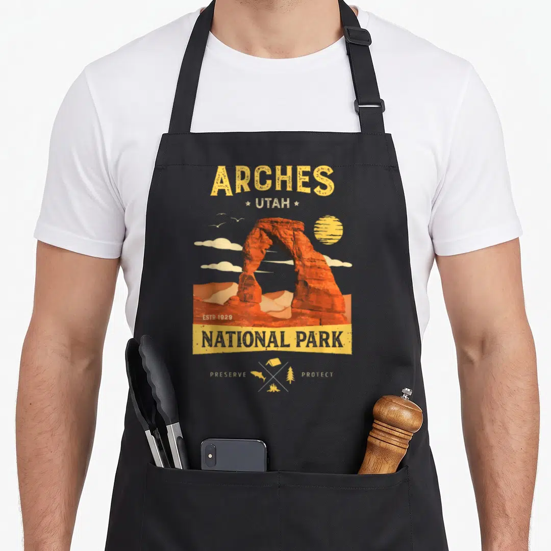 Arch backpacking apron - Vintage Arches National Park rock arch with sun, clouds, and camping icons in yellow orange — shown on a black cotton canvas apron against a white background