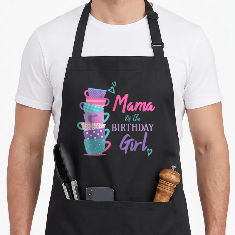 Mama tea party aprons - Stack of six patterned teacups in pink purple teal and lilac next to Mama Of the Birthday Girl — shown on a black cotton canvas apron against a white background