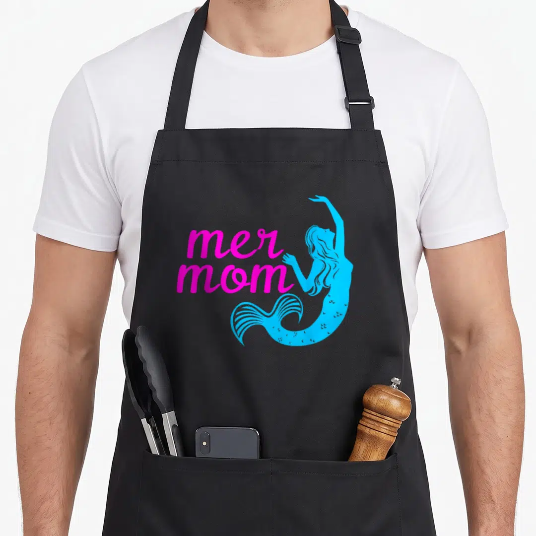 Mer fish apron - Stacked magenta mer mom text beside a blue mermaid silhouette — shown on a black cotton canvas apron against a white background