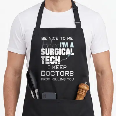 Surgical doctor apron - Stacked white and blue text reading BE NICE TO ME I'M A SURGICAL TECH with EKG line and scalpel — shown on a black cotton canvas apron against a white background
